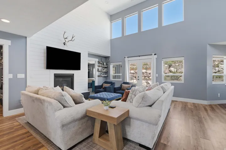 Vaulted ceiling with high transom windows, wood-finish flooring, fireplace with white shiplap surround, and white French doors