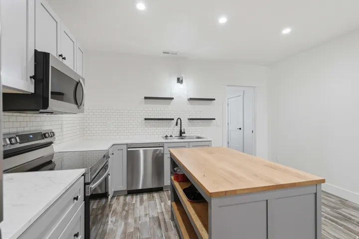 Kitchen featuring wood-finish flooring, white subway tile backsplash, light grey cabinetry, stainless steel appliances, and a beautiful butcher block island