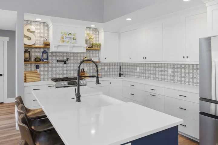 White shaker cabinetry with matte black hardware, stainless steel appliances, a center island with a light-toned countertop, a patterned tile backsplash, and wood-finish flooring