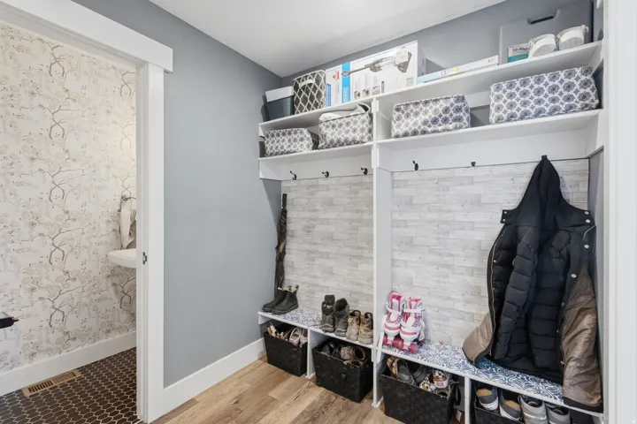 mudroom featuring built-in white cabinetry with open shelving, multiple hooks for outerwear storage, woven basket organizers, and wood-finish flooring