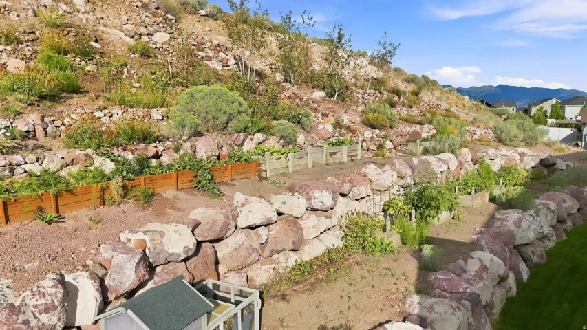 Tiered landscaping with natural rock retaining walls, multiple raised garden beds, and sloped terrain with natural vegetation