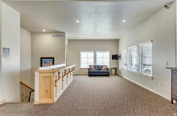 Spacious room featuring multiple windows, recessed lighting, carpet flooring, and a wood-finish railing