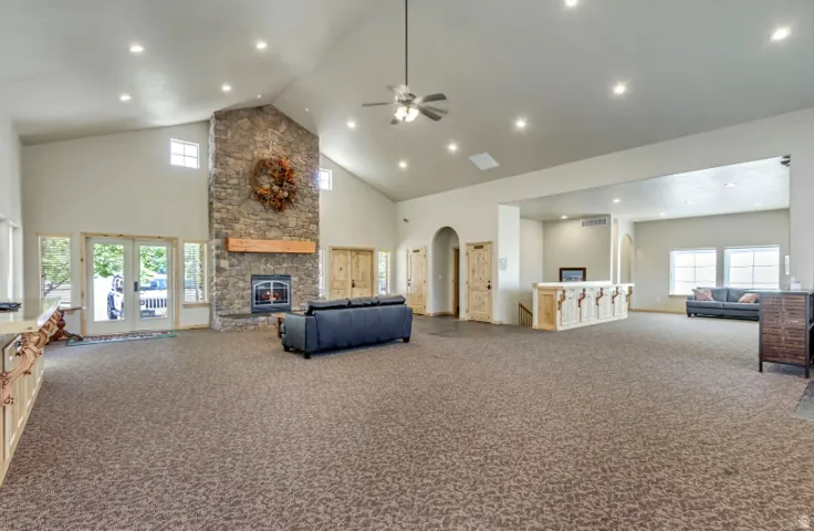 Vaulted ceilings with recessed lighting, stone fireplace with a wood mantle, double French doors, built-in bar, and arched doorways