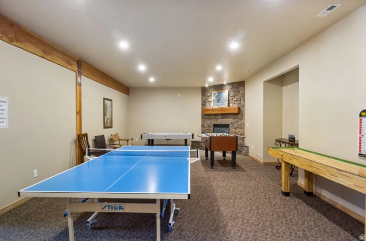 Recreational basement featuring a regulation-size ping pong table, shuffleboard court, wood-beam ceiling detail, recessed lighting, carpet flooring, and a fireplace with stone surround