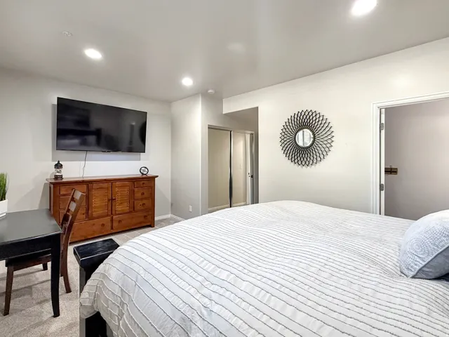 Spacious primary suite with king bed, desk space, beautiful furniture, mounted smart TV, and ensuite bath with double vanity, gorgeous granite countertops, and knotty alder cabinets.