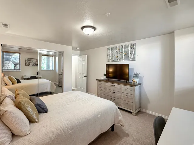 Bedroom 2 located in the basement with beautiful furnishings, queen bed, large smart TV, and desk space for working.