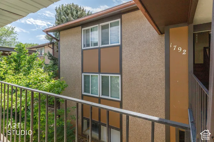 Stucco exterior with contrasting trim, multiple windows featuring blinds, and a metal balcony railing