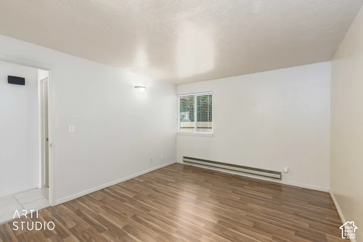Wood-finish flooring with white baseboards, a wall-mounted light fixture, and a window with blinds
