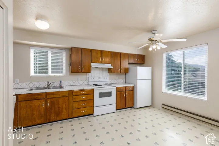 Kitchen featuring wood cabinetry, white tile backsplash, double-basin sink, white range, and ceiling fan