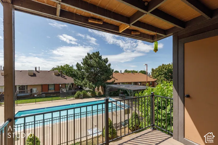 Balcony featuring a black metal railing and wood-finish ceiling, overlooking a fenced swimming pool with a surrounding patio