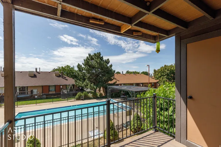 Balcony featuring a black metal railing and wood-finish ceiling, overlooking a fenced swimming pool with a surrounding patio