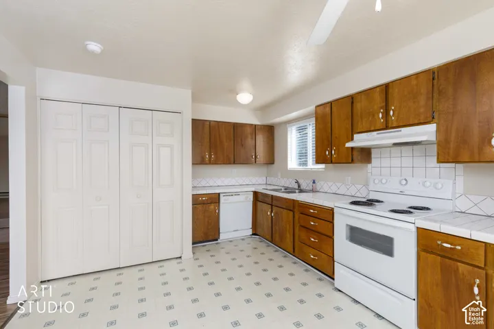 Kitchen featuring wood cabinetry, white tile countertops, white tile backsplash, and a built-in white dishwasher