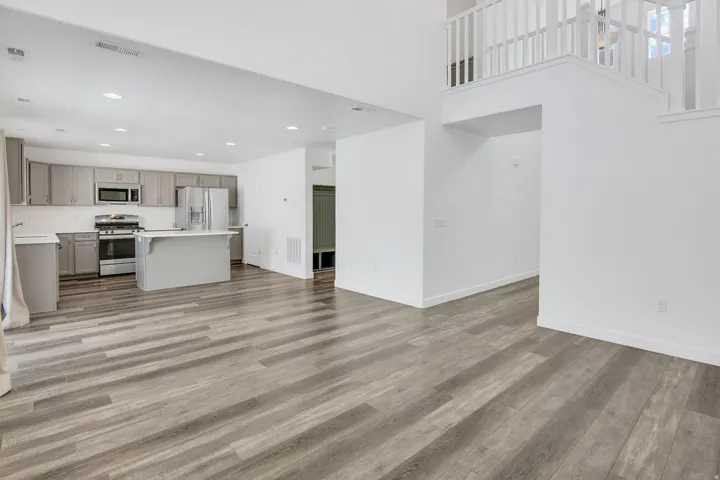 Open-concept living area featuring wood-finish flooring, a kitchen with grey cabinetry, a center island, stainless steel appliances, and a white balustrade overlooking the space