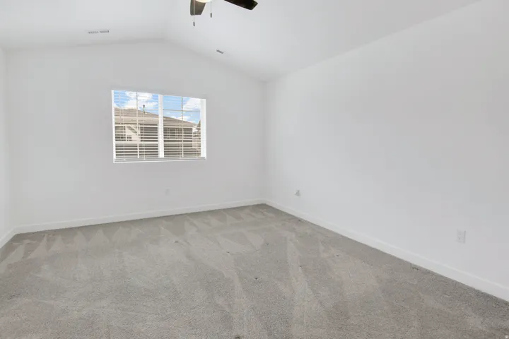 Vaulted ceiling with a ceiling fan, neutral gray carpeting, and a window with blinds