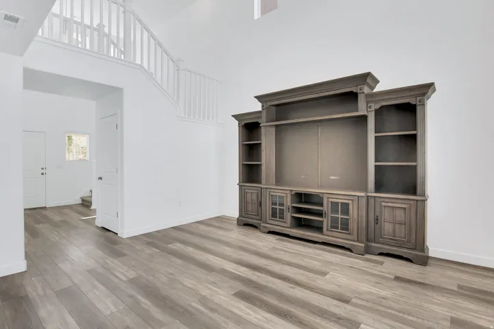 Wood-finish flooring throughout, white painted walls, white railing staircase, and a built-in media console