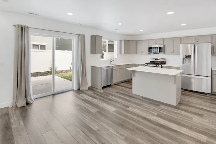 Spacious room featuring wood-finish flooring, a kitchen with gray cabinetry and white countertops, stainless steel appliances, a kitchen island, and a sliding glass door
