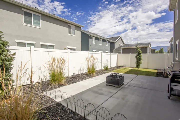 Expansive backyard featuring a concrete patio, fenced perimeter, and landscaped beds with ornamental grasses