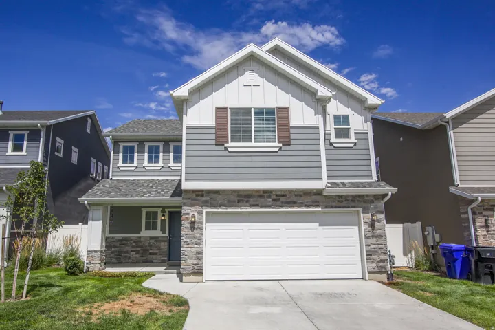 Stone veneer facade, two-car garage, white framed windows, gray siding, and brown shutters