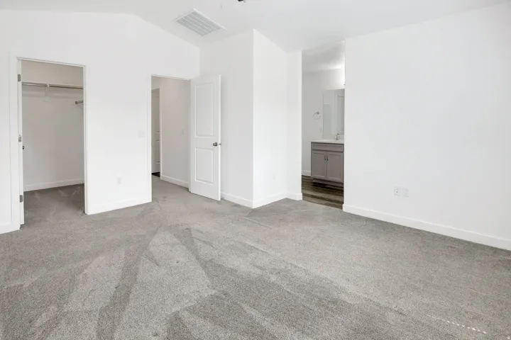 Plush gray carpeting, white painted walls, and a built-in closet with shelving and hanging rods