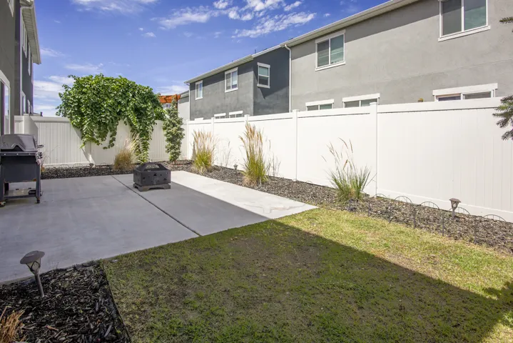 Expansive concrete patio with a surrounding white privacy fence, complemented by mature landscaping and decorative rock beds