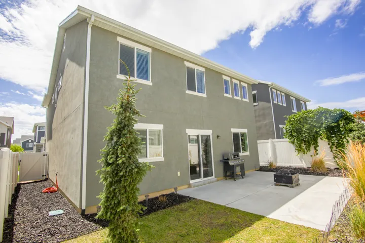 Rear exterior featuring a concrete patio, sliding glass door access, multiple windows, and a white fence