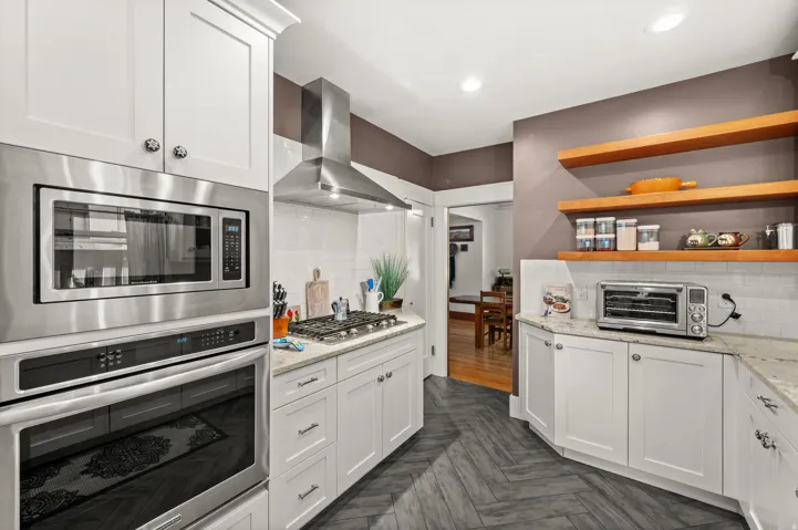 White shaker-style cabinetry with integrated stainless steel appliances, granite countertops, and a white subway tile backsplash