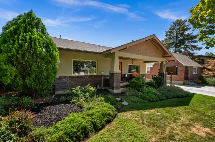 Stucco exterior with brick detailing, covered front porch, gabled roofline, and landscaped front yard