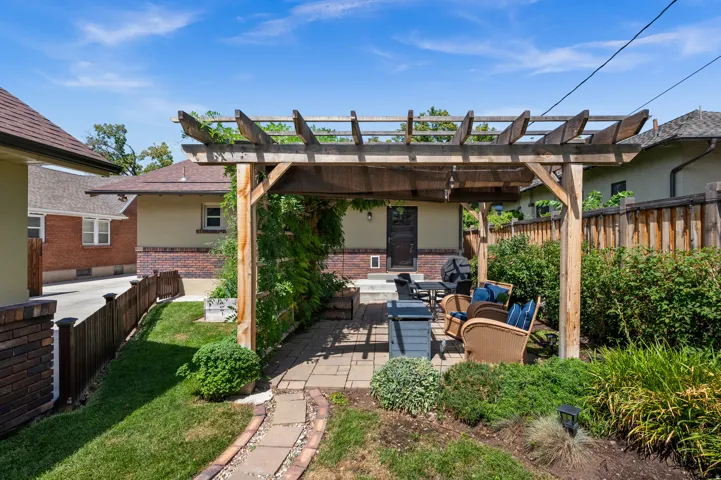 Expansive outdoor patio featuring a wood pergola, paver flooring, and mature landscaping