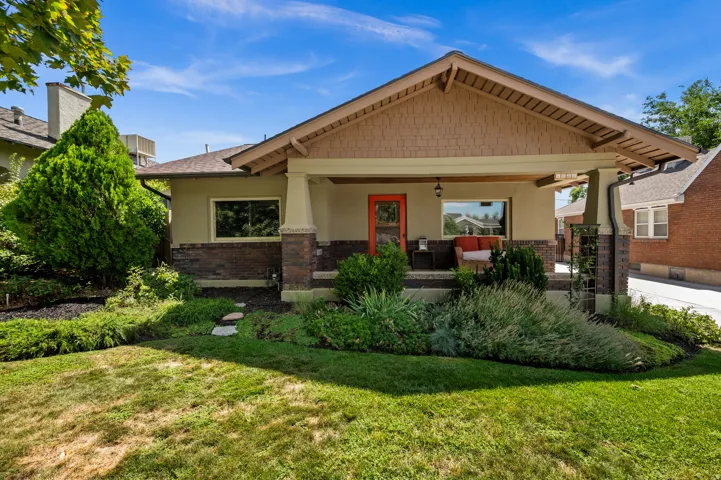 Craftsman-style home featuring a covered front porch, decorative gable shingles, a prominent brick base, and mature landscaping