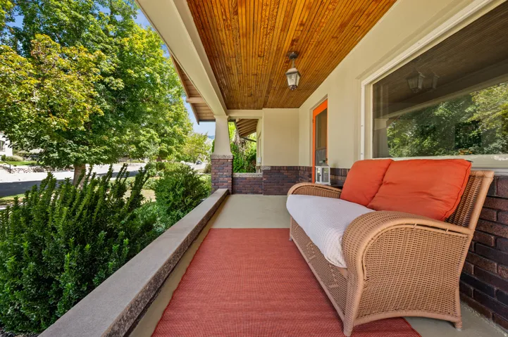Covered front porch featuring a wood-finish ceiling, brick detailing, and an exterior light fixture