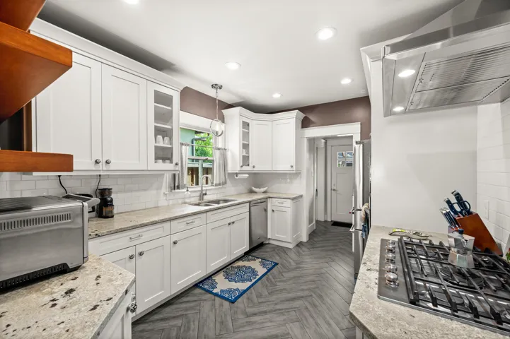 White cabinetry with silver hardware, light-toned countertops, white subway tile backsplash, and herringbone wood-finish flooring