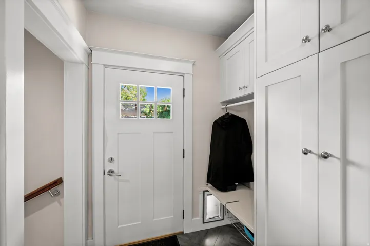 White shaker cabinetry with chrome hardware, built-in shelving, glass-paned door, and wood-finish flooring