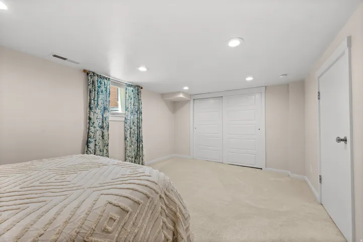 Recessed ceiling lighting, light-colored carpeting, white walls, built-in sliding closet doors, and an egress window