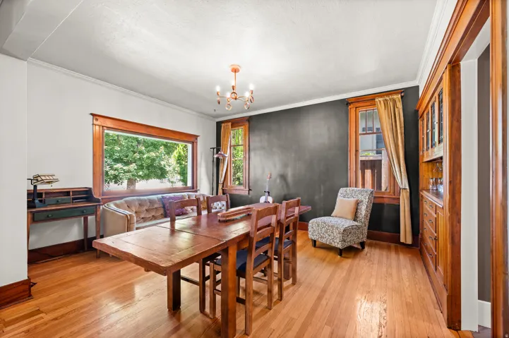 Hardwood flooring throughout, featuring a large picture window, crown molding, and a built-in wooden display cabinet