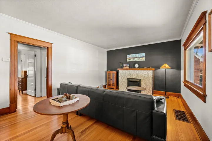Hardwood flooring, cased entryway, fireplace with decorative tile surround, crown molding, and wood-trimmed window