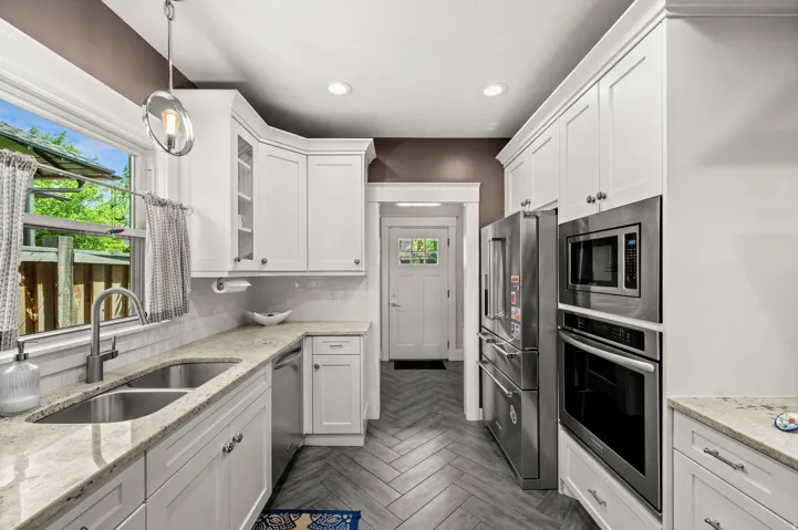 Kitchen featuring white shaker-style cabinetry, light-toned countertops, stainless steel appliances, and herringbone-patterned flooring