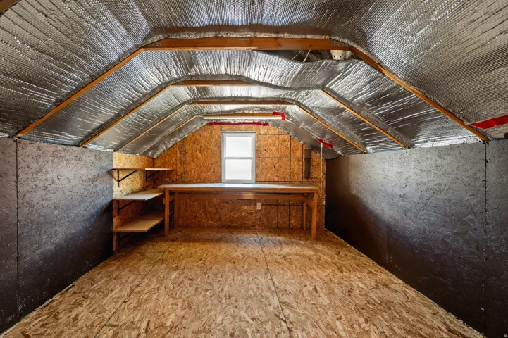 Attic space featuring pitched ceiling with insulation, wood-finish flooring, built-in shelving, and a built-in workbench