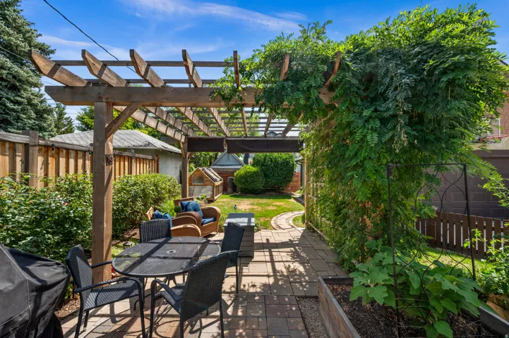 Expansive backyard featuring a wood pergola, paver patio, established plantings, and a winding stone pathway
