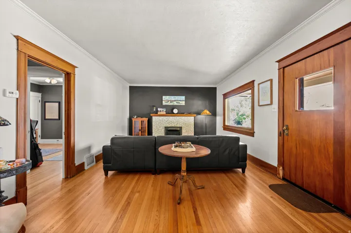 Hardwood flooring, wood trim, white crown molding, fireplace with tiled surround, and a built-in window