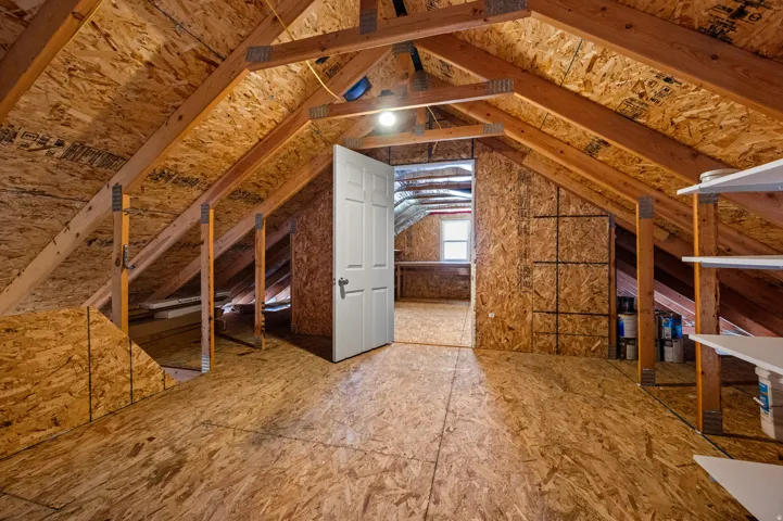 Attic space featuring exposed wood framing, oriented strand board walls, and a paneled door