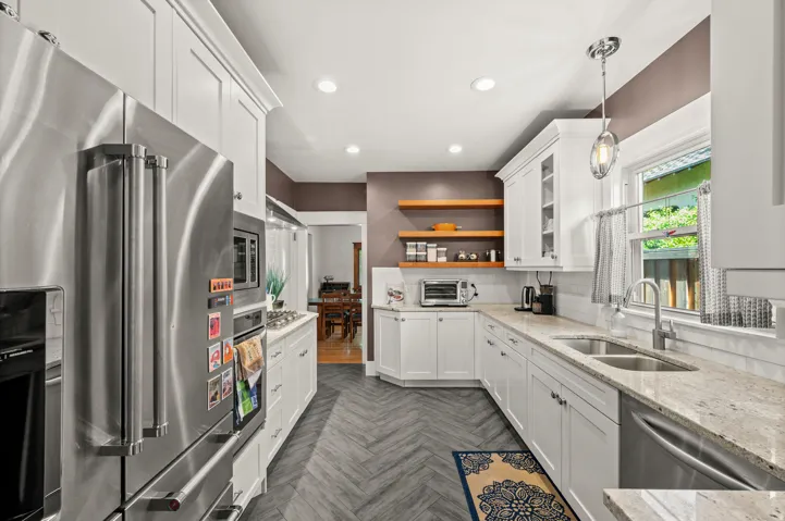 White cabinetry, stainless steel appliances, herringbone-patterned flooring, light-toned countertops, and open shelving
