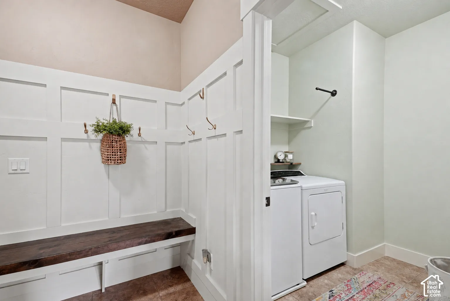 Mudroom featuring wainscoting, a built-in wooden bench, integrated coat hooks, and an adjacent laundry area with built-in shelving