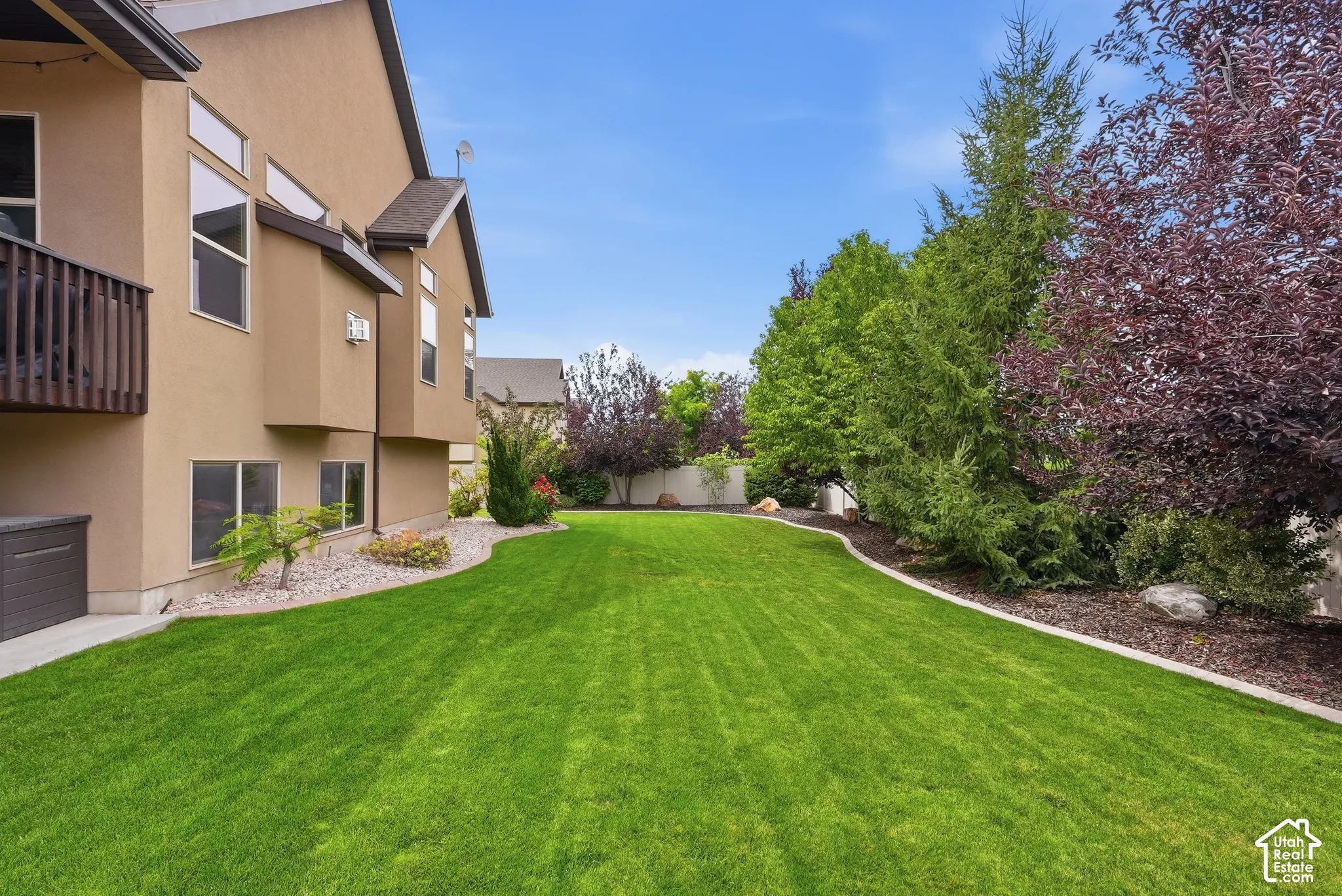 Expansive lawn area with a defined landscape border, mature trees, and a multi-level exterior with a wooden balcony
