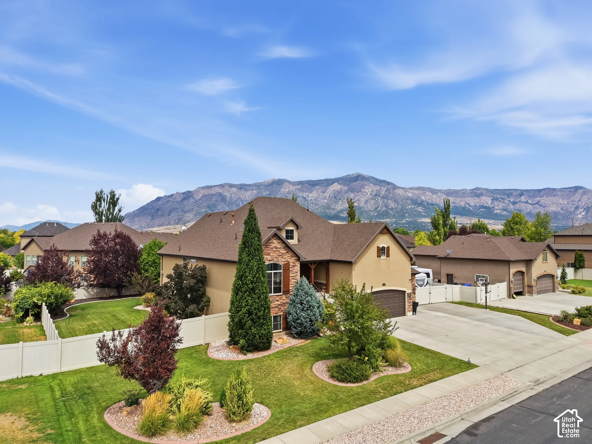 Exterior showcasing a stone and stucco facade, a multi-car driveway, and a fenced backyard with landscaped greenery