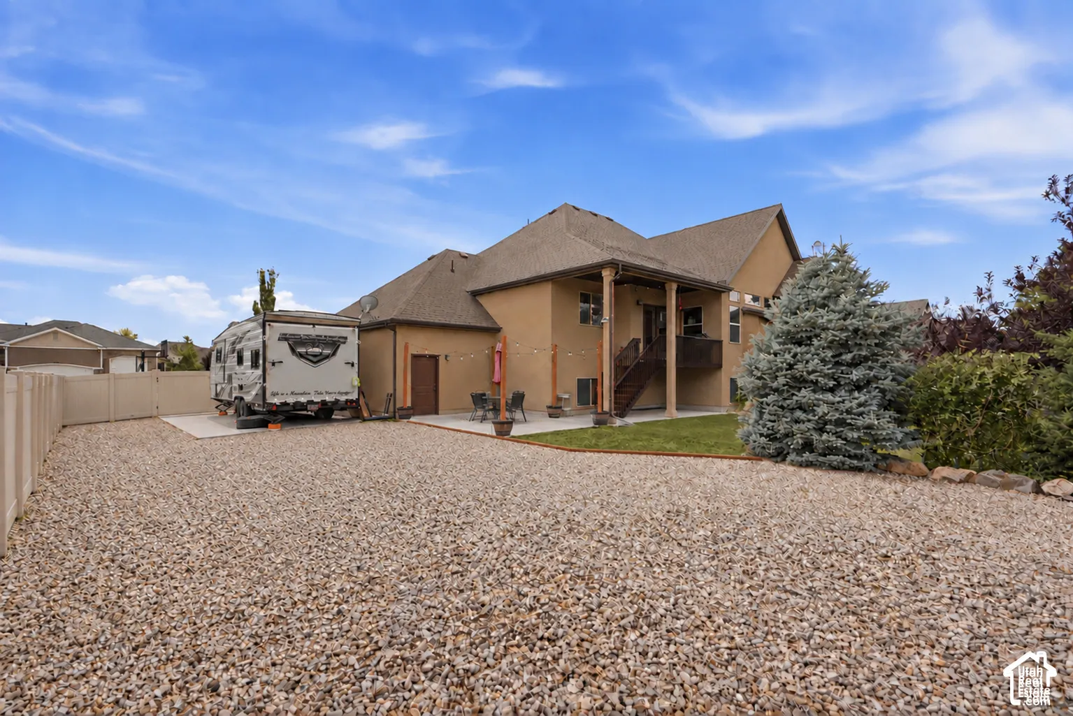 Exterior rear elevation featuring a stucco facade, expansive gravel side yard, paved patio, and tall privacy fencing