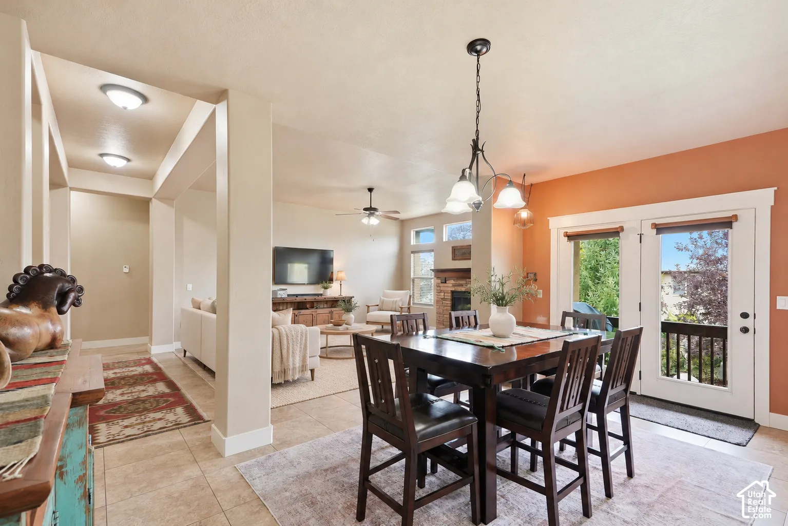Open-concept interior featuring neutral wall tones, stone-finish tile flooring, a multi-arm chandelier, an inset stone fireplace, and double-paned glass garden doors
