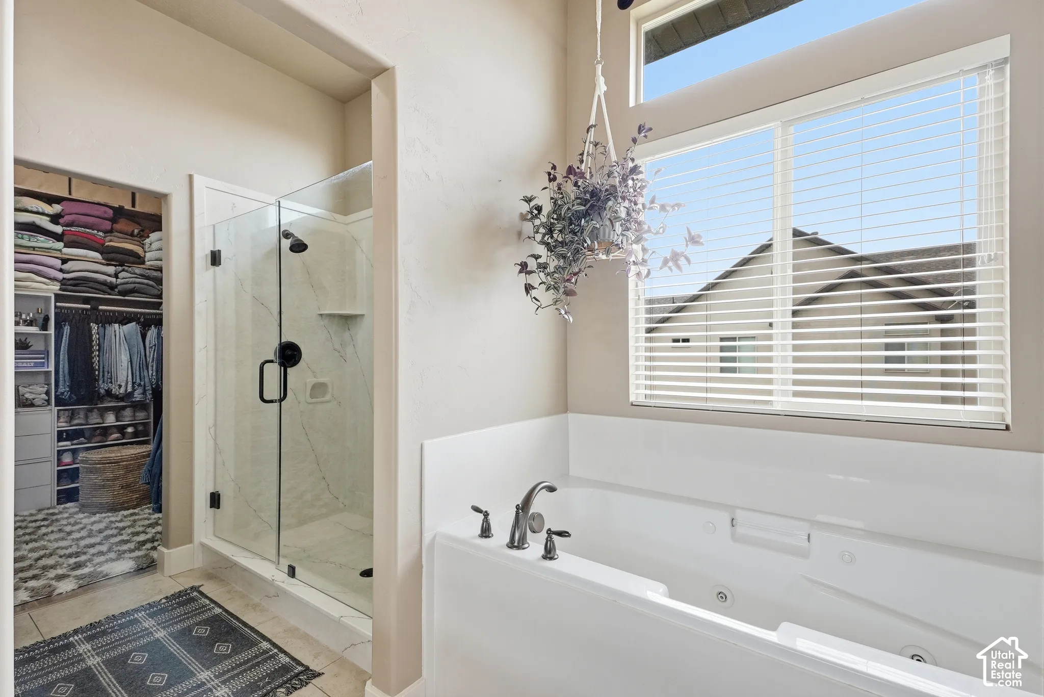 Built-in soaking tub with dark-finish fixtures, clear glass shower enclosure with dark-finish hardware, organized walk-in closet, and an upper transom window