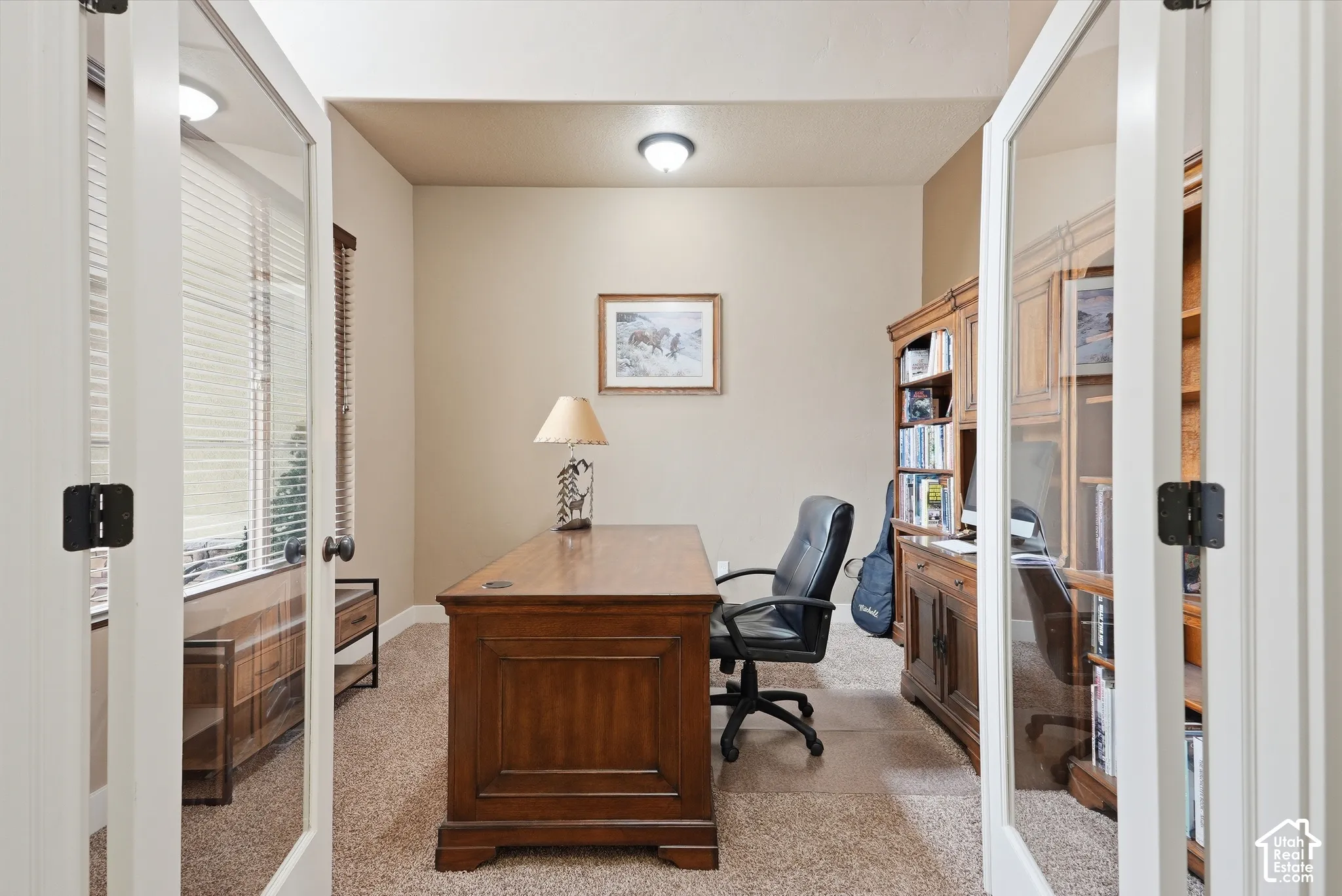 Room accessed by two glass-paneled doors, featuring neutral-toned walls, textured carpet flooring, and a ceiling-mounted light fixture