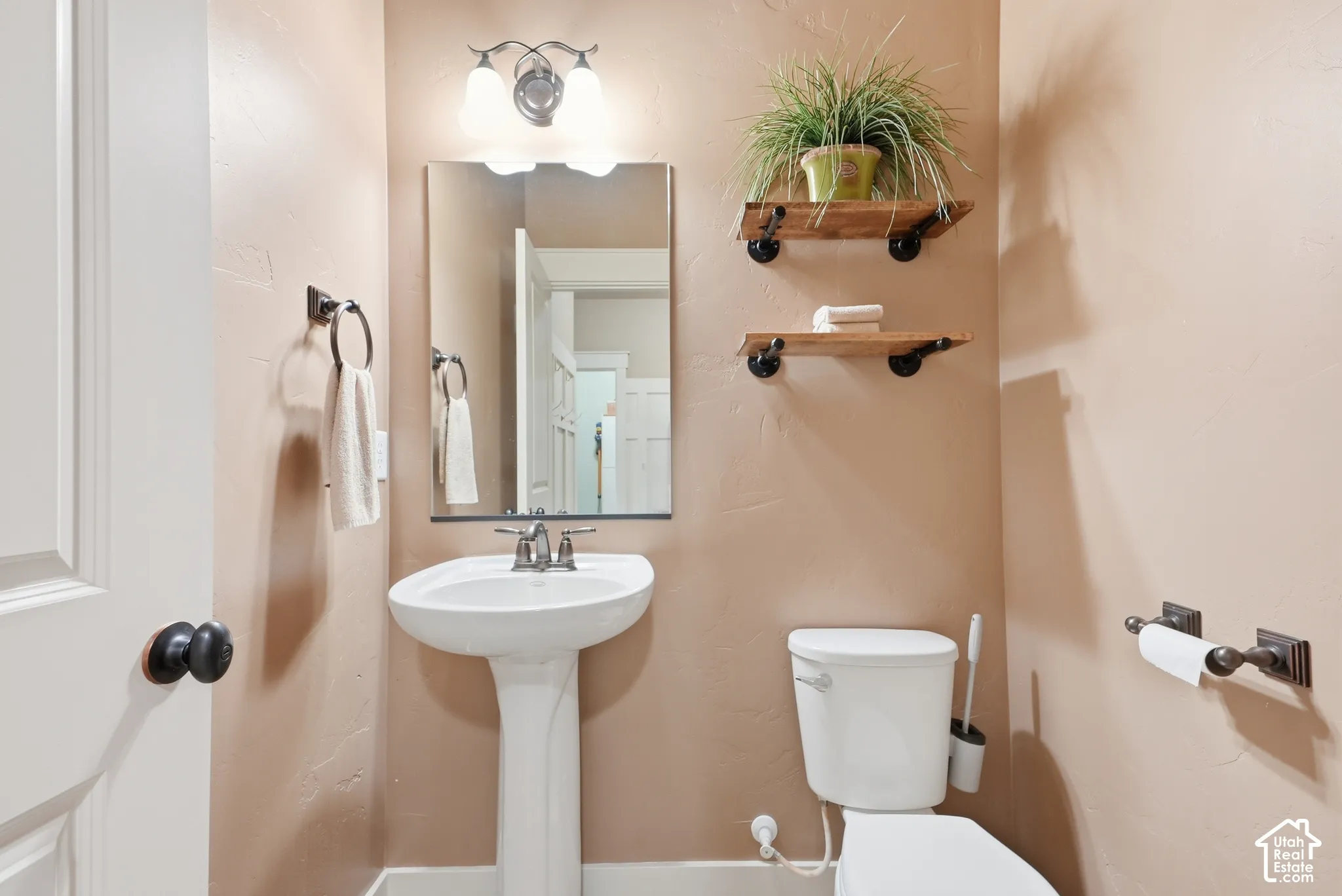 Pedestal sink with a coordinating wall-mounted mirror, two-light vanity fixture, and industrial-style shelving