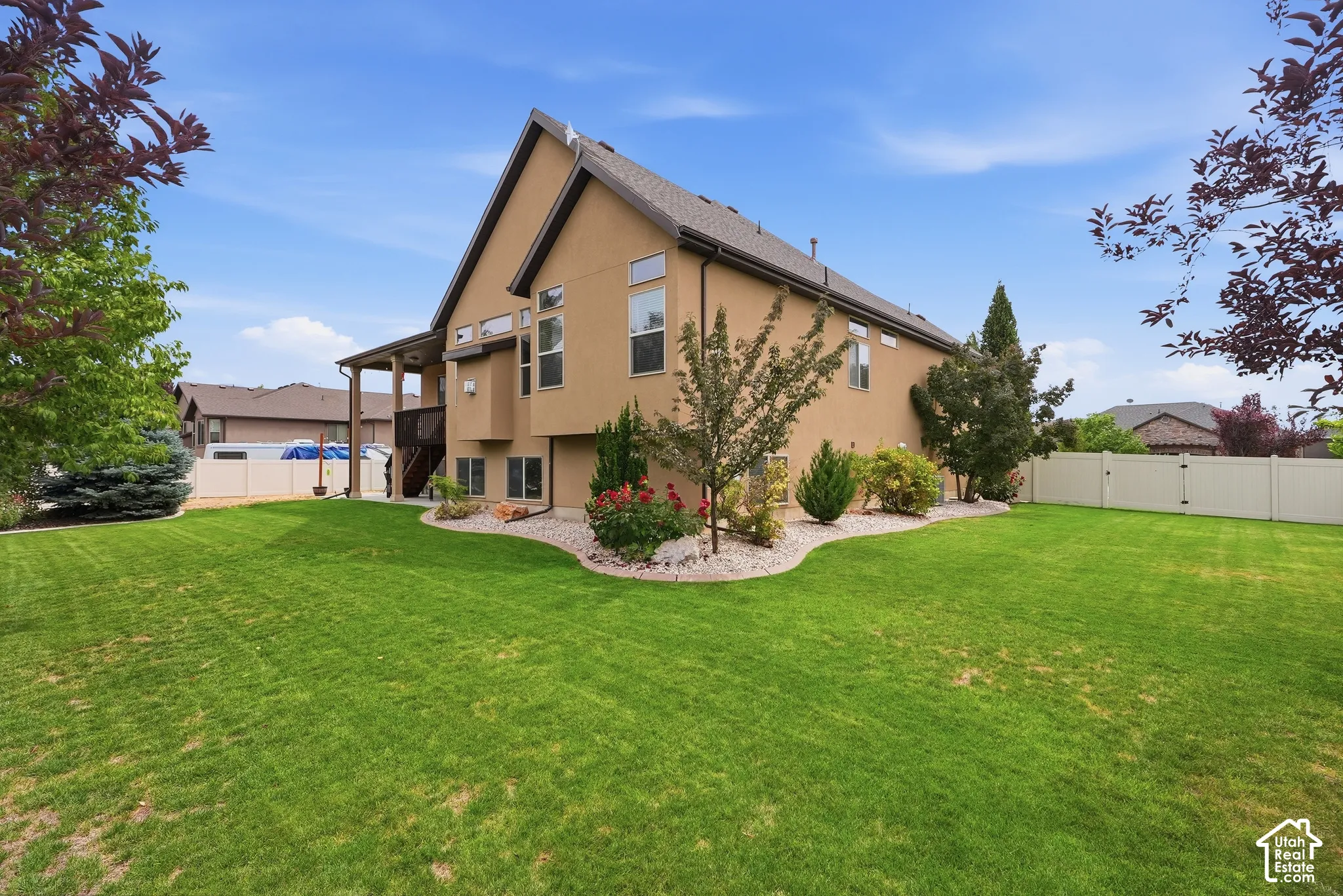 Expansive backyard featuring a manicured lawn, established landscaping, and a tan vinyl fence